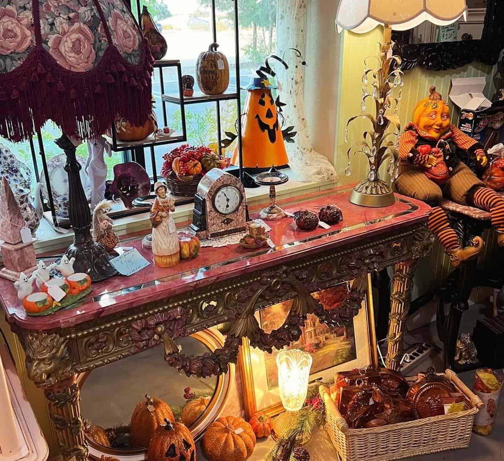 Colorful Halloween-themed decorations and figurines displayed on an ornate table in an antique shop.