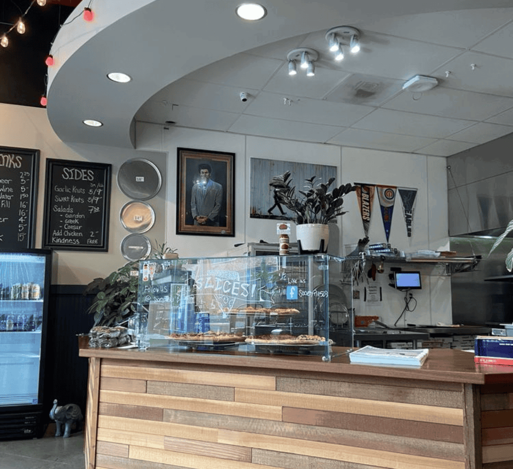 Fresh pizza at QuestForDirections restaurant counter with interior decor, menu, and plants.