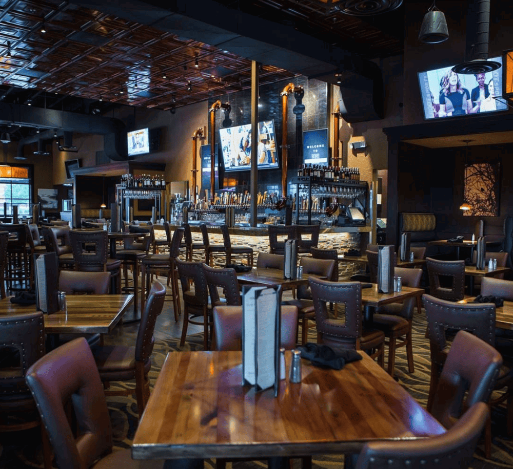 Modern sports bar interior with multiple TVs and craft beer taps for outdoor dining and live sports entertainment.