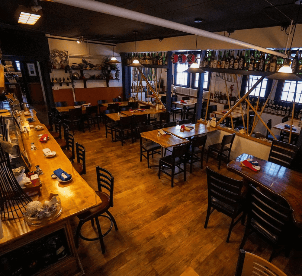 Cozy Japanese restaurant interior with wooden tables, sake bottles, and traditional decor.