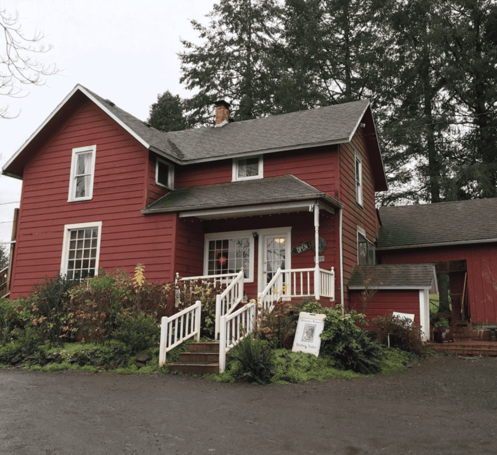 Cozy red house with white trim, lush garden, and welcoming front porch, ideal for a charming stay.