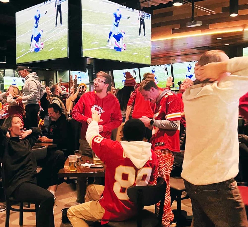 Excited fans watching football game on multiple screens at a sports bar.