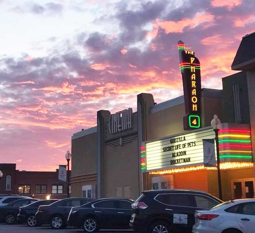 Brightly lit marquee theater showcasing classic films at sunset with colorful sky background.