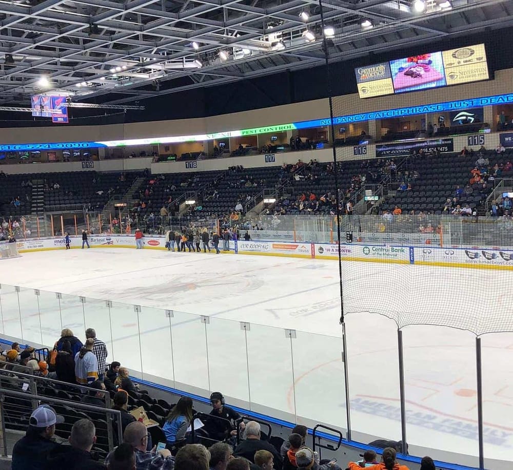 Ice hockey arena interior, seating, scoreboard, with spectators and players preparing for game.