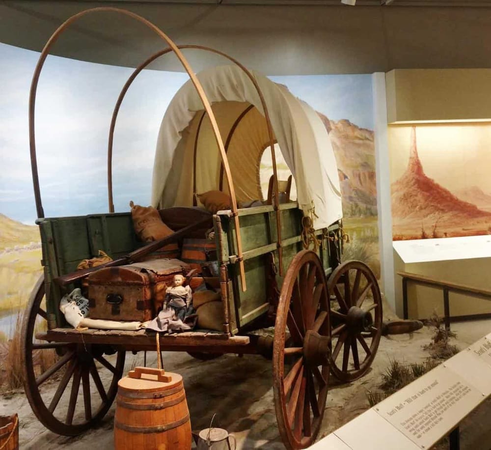 Covered wagon with historical artifacts at a museum exhibit, showcasing pioneer transportation and Westward Expansion history.