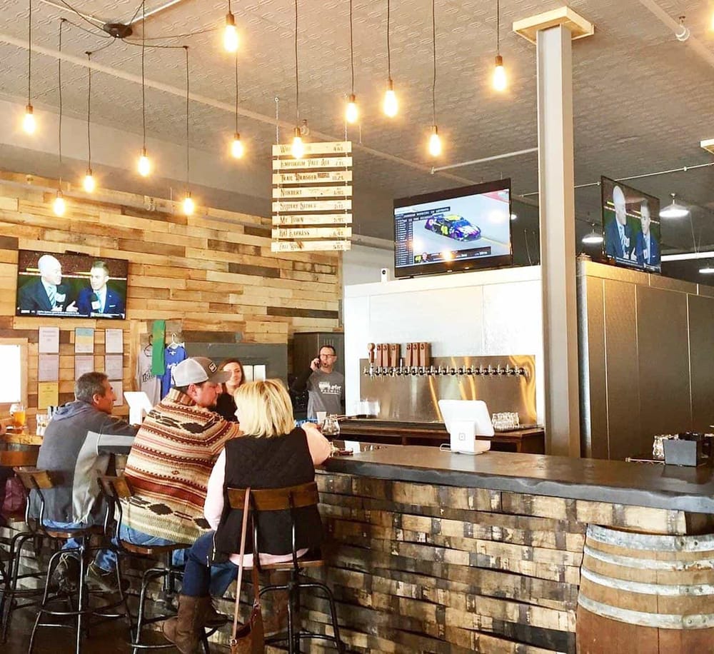 Cozy sports bar with multiple TV screens showing racing and news, wooden decor, and inviting seating area for fans and patrons.