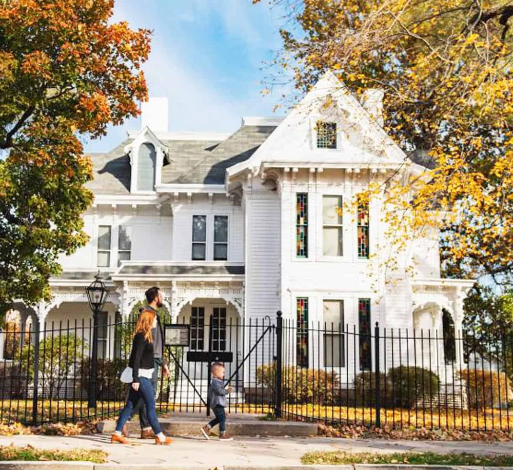 Elegant Victorian house with colorful stained glass windows, surrounded by autumn trees.