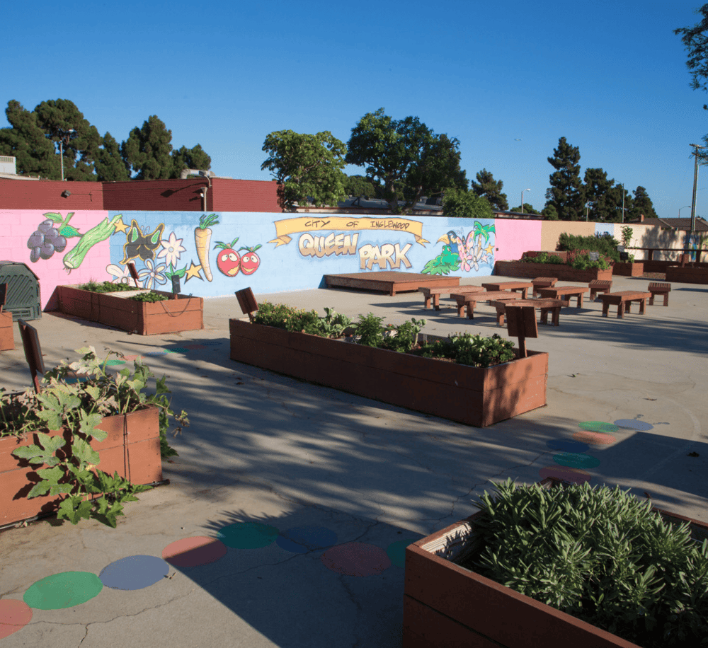 Bright Queen Park mural in Inglewood, California, with flower planters and outdoor seating areas.
