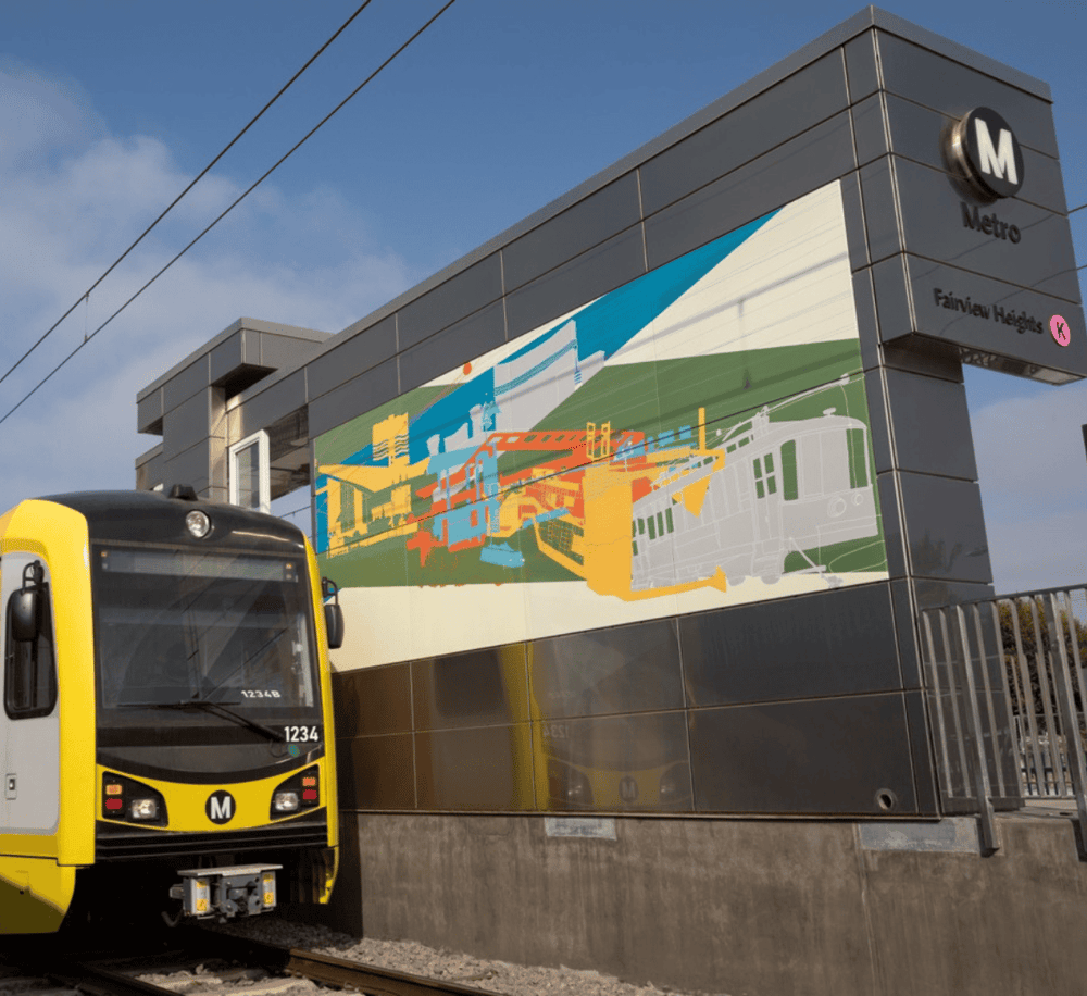 Bright yellow metro train at a modern metro station with colorful urban art mural in the background.