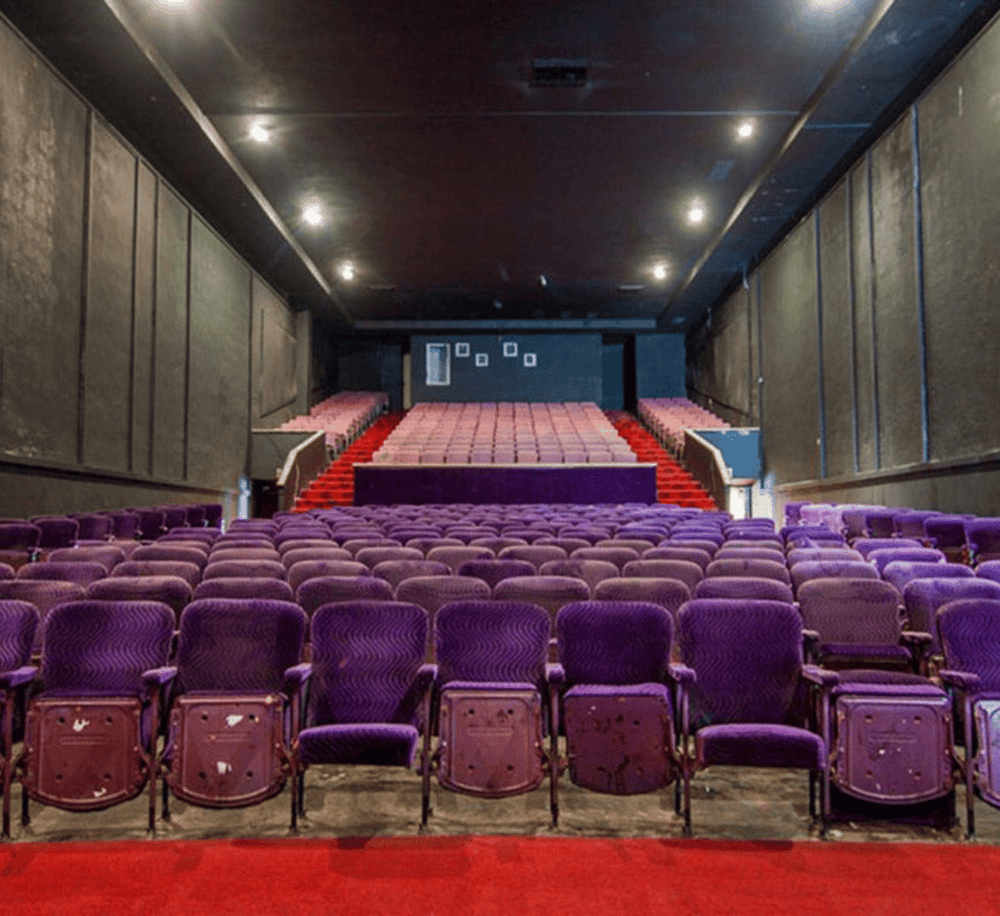 Comfortable theater seating with purple upholstery and tiered stage for live performances or film screenings.
