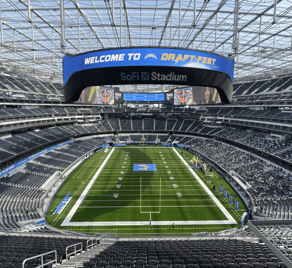 Bright stadium interior with football field, large digital screens, and seating at SoFi Stadium in Los Angeles.