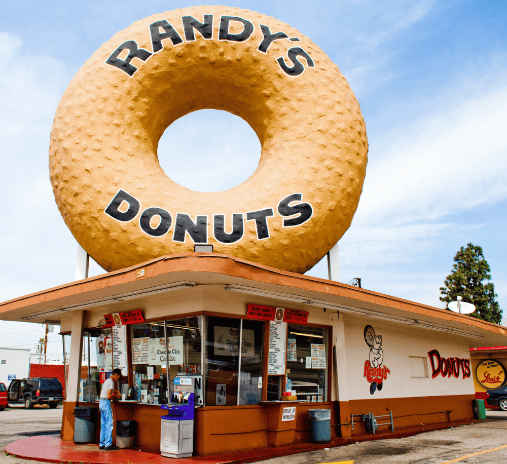 Vast donut shop with giant donut sign, colorful storefront, and classic American fast-food atmosphere.