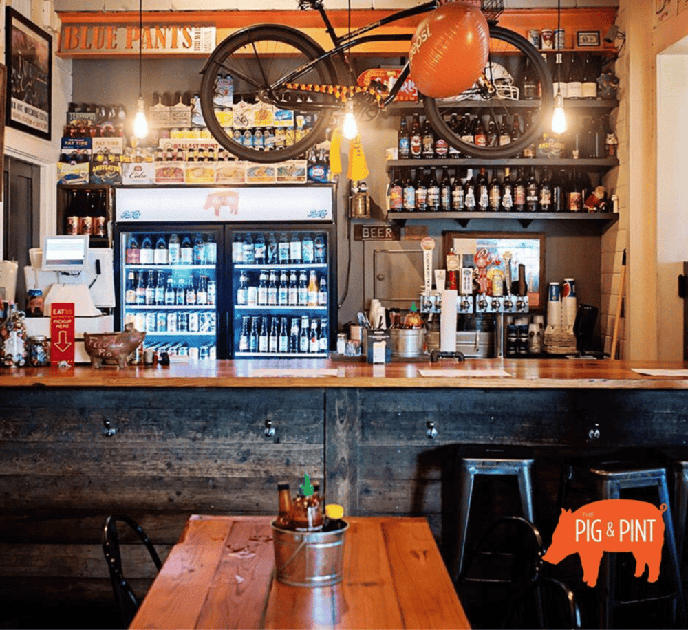 Oak bar with beer bottles and vintage decor at the Pig & Pint pub.
