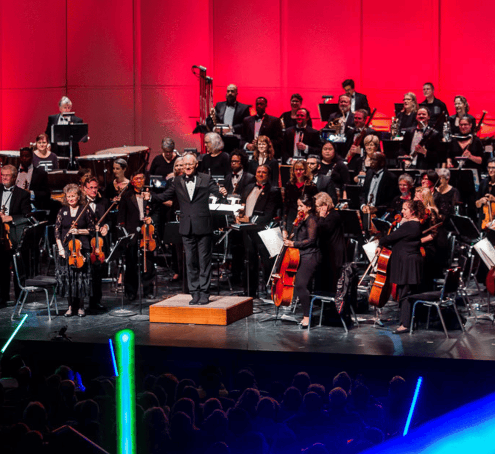 Orchestra performing live at a concert hall for a musical event with a conductor and diverse musicians.