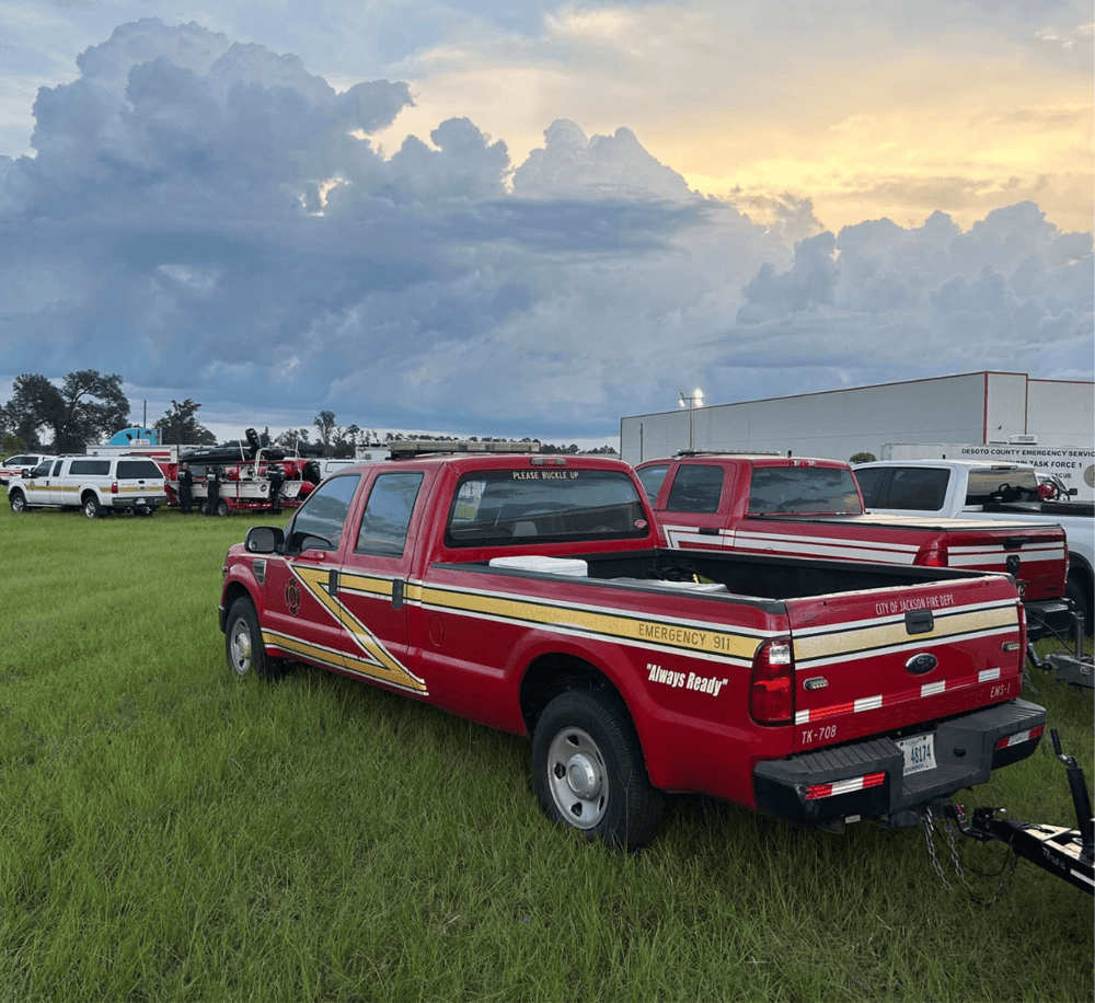 Emergency response vehicle parked on a grassy field with cloudy sky overhead.