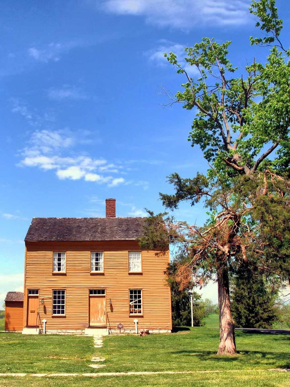 Old wooden house with tree under clear blue sky, historical site, rural building, American heritage, architecture.