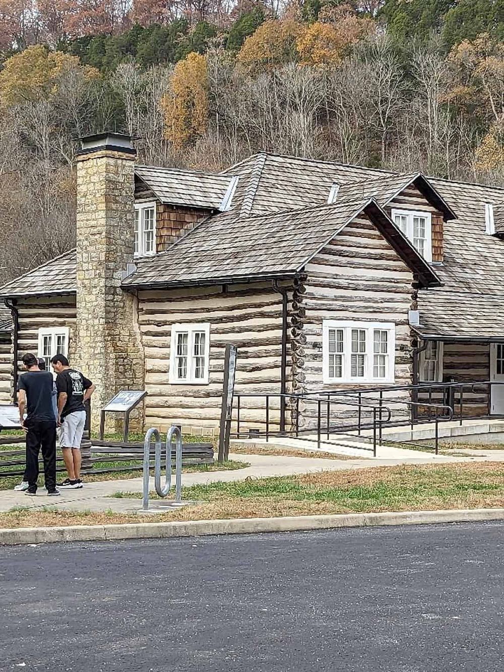 Old log cabin museum with a stone chimney and autumn forest backdrop, showcasing historic American architecture.