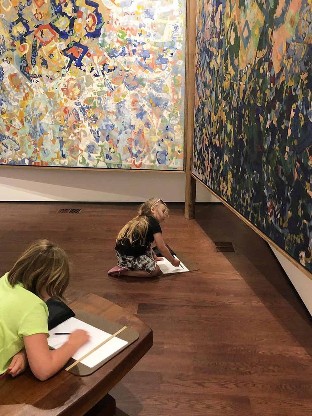 Vibrant abstract art exhibit with children sketching and observing colorful paintings, educational art experience for kids.