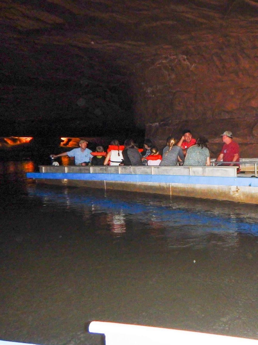 Colorful boat touring through a dark, scenic cave with people enjoying the adventure.