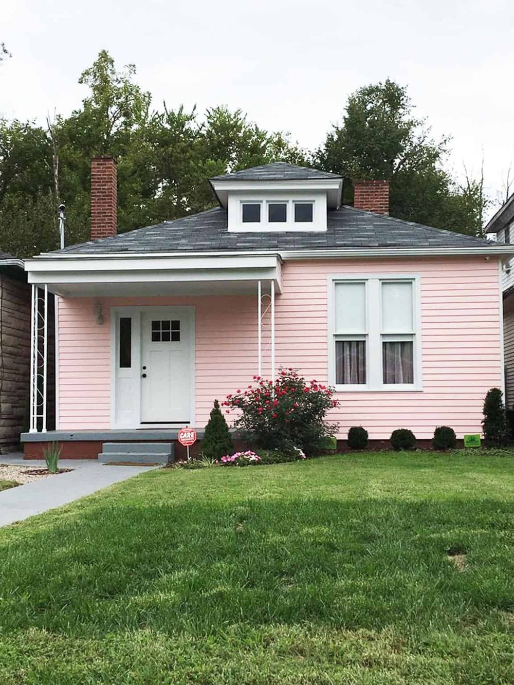 Charming pink house with a front porch and well-maintained lawn, perfect for homeownership.