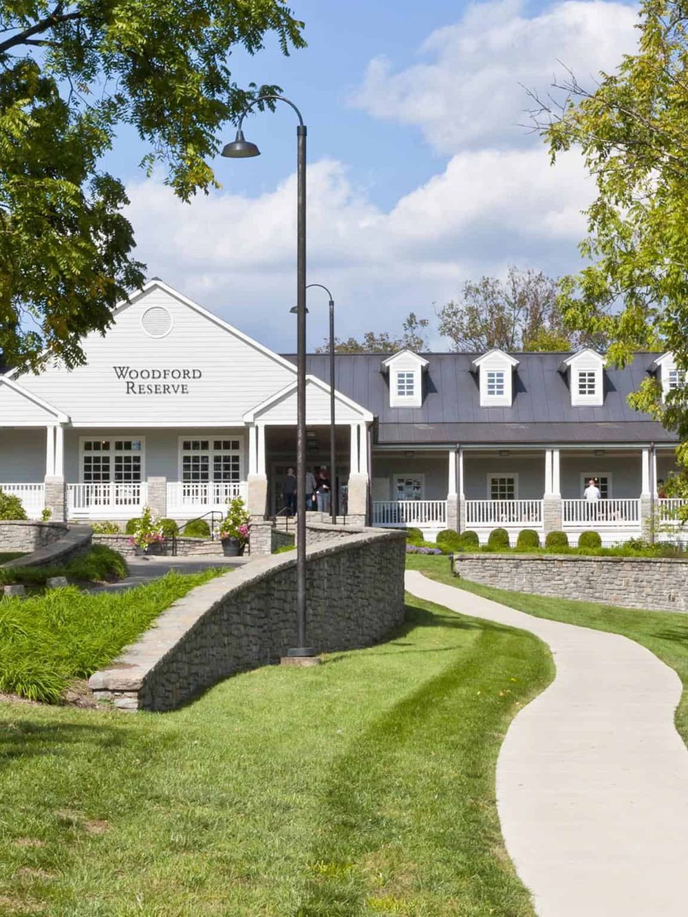 Lush green park at Woodford Reserve with walking path and historic building in the background.