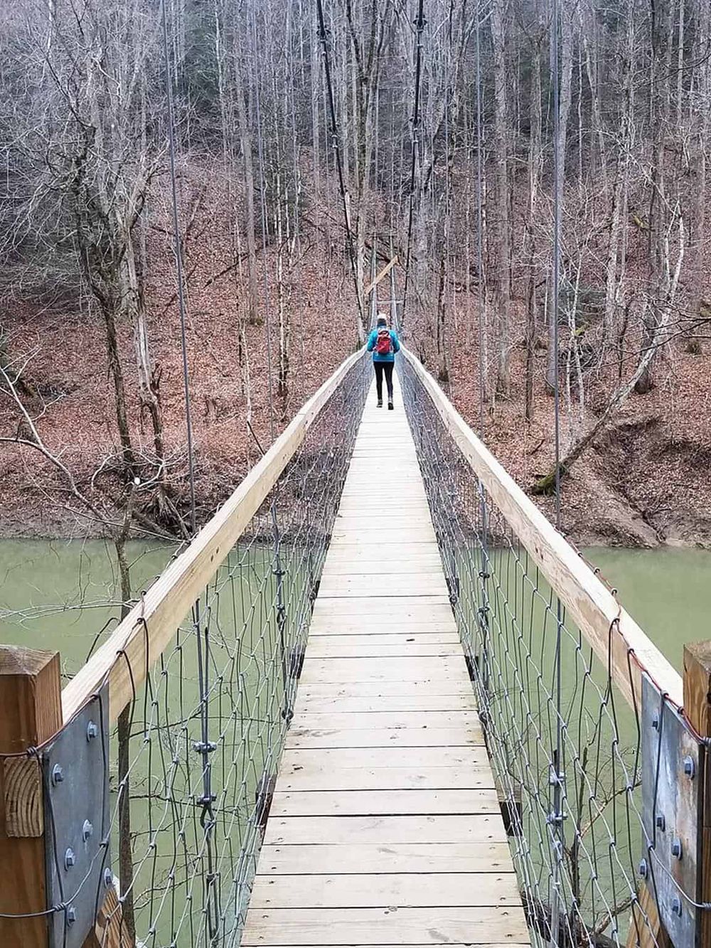 Suspension bridge over river in wooded area for outdoor adventure and hiking.