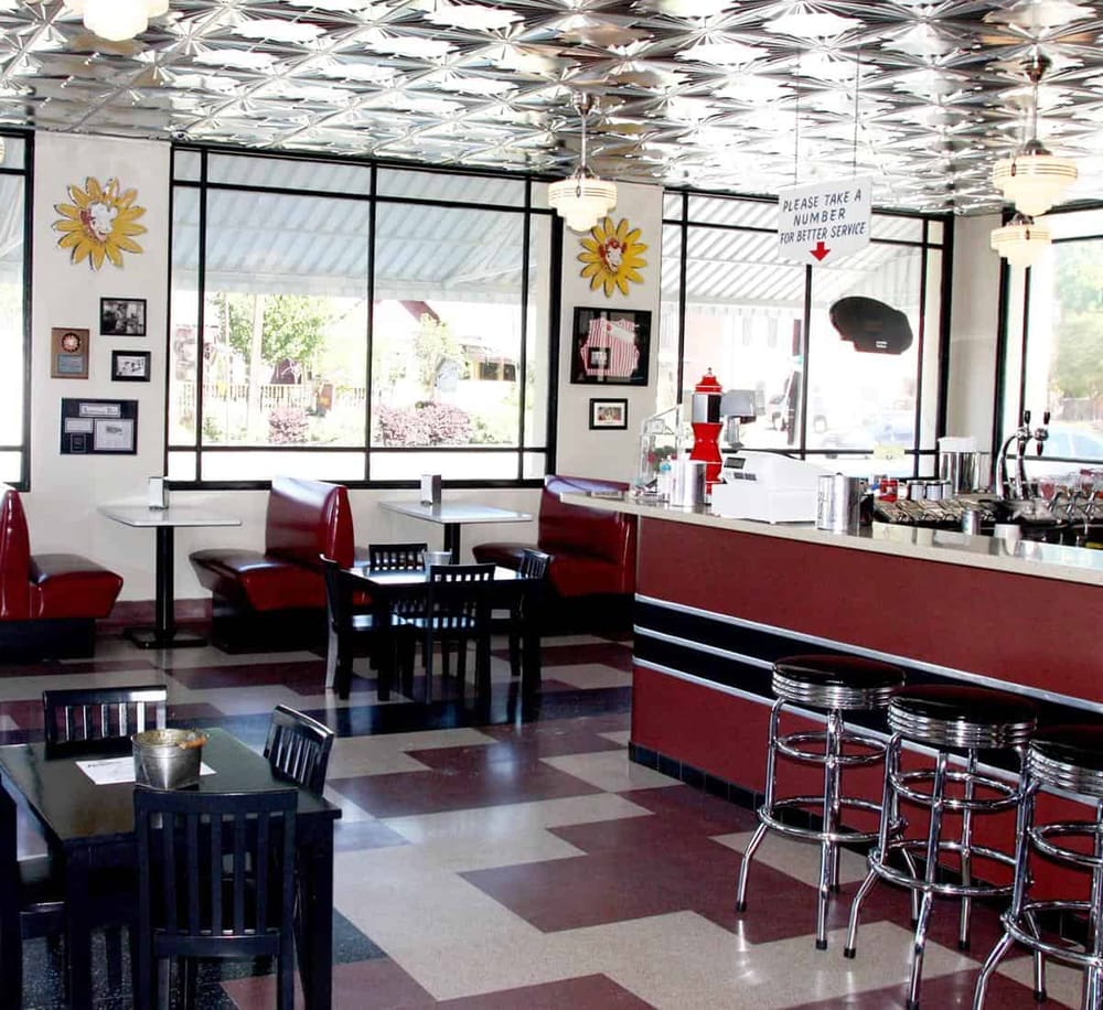 Bright retro-style diner interior with red booths, black tables, and checkered flooring, showcasing a classic American restaurant vibe.