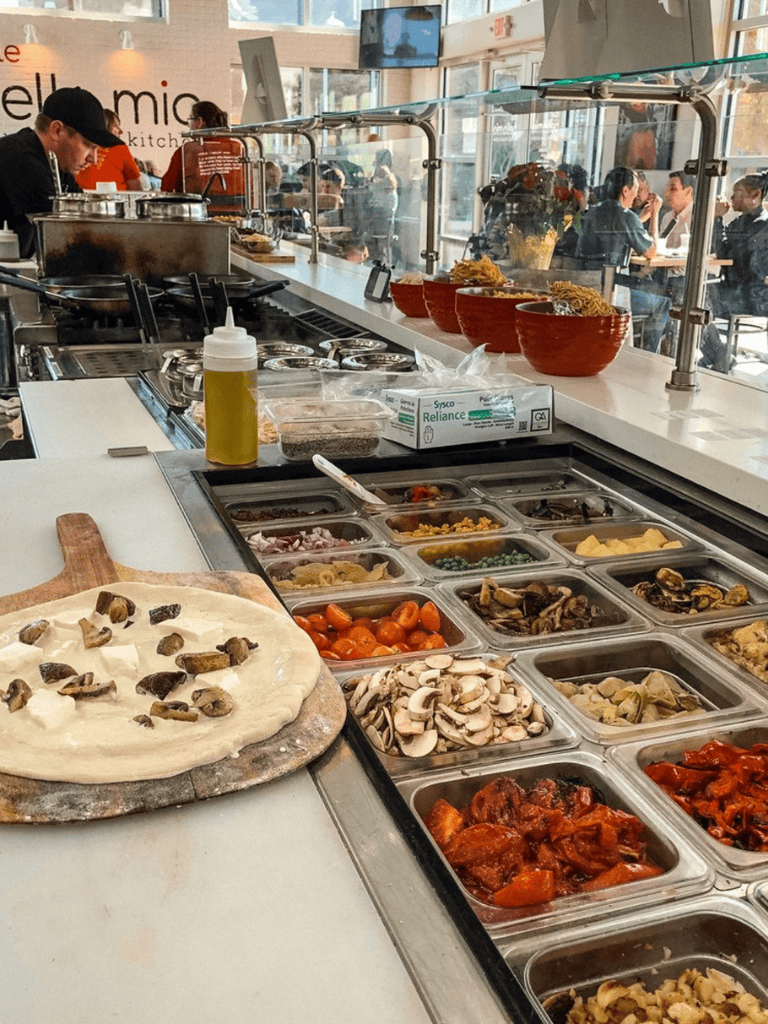 Fresh pizza ingredients and toppings at a busy restaurant buffet.