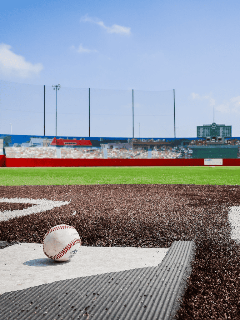 Baseball on home plate at a stadium with bright blue sky and stands in the background.