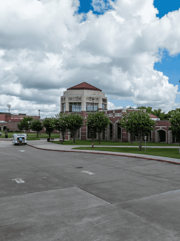 Modern brick building with a round tower and lush trees, under a partly cloudy sky, at QuestForDirections.