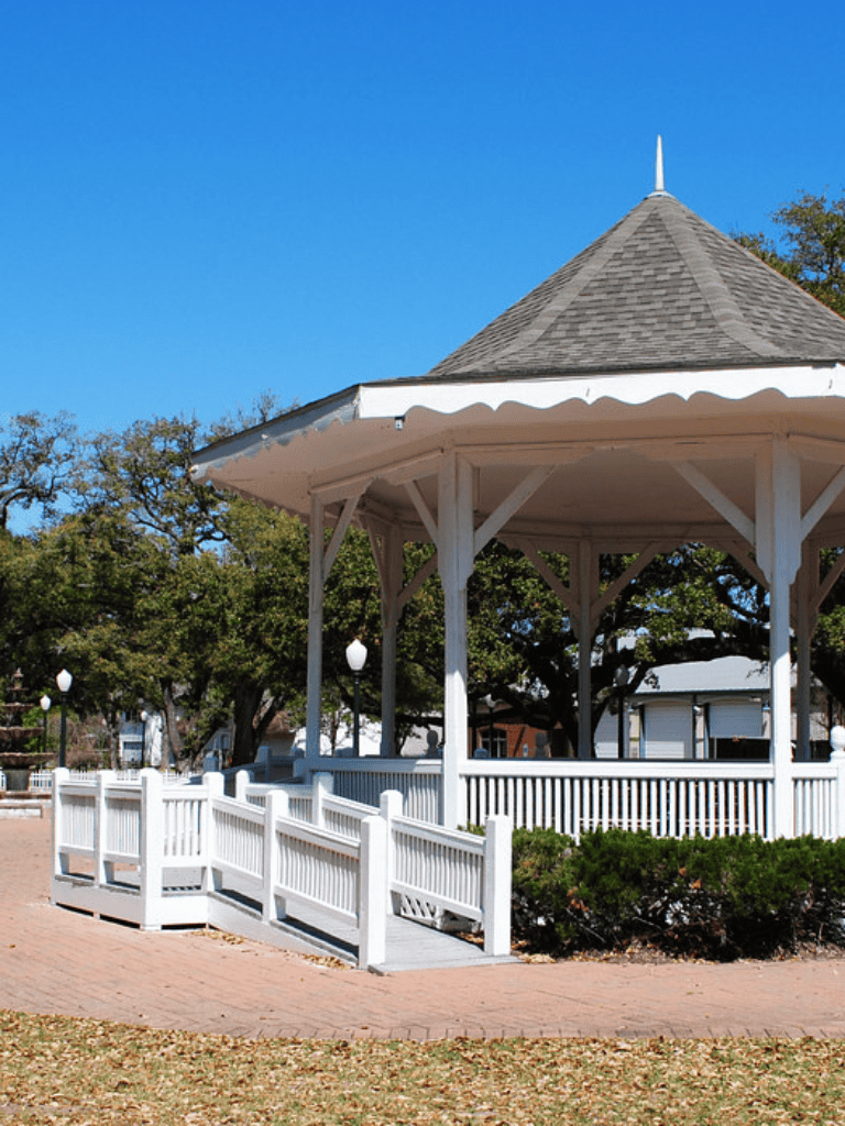 Quaint white gazebo in park with surrounding trees, perfect for outdoor gatherings and events.