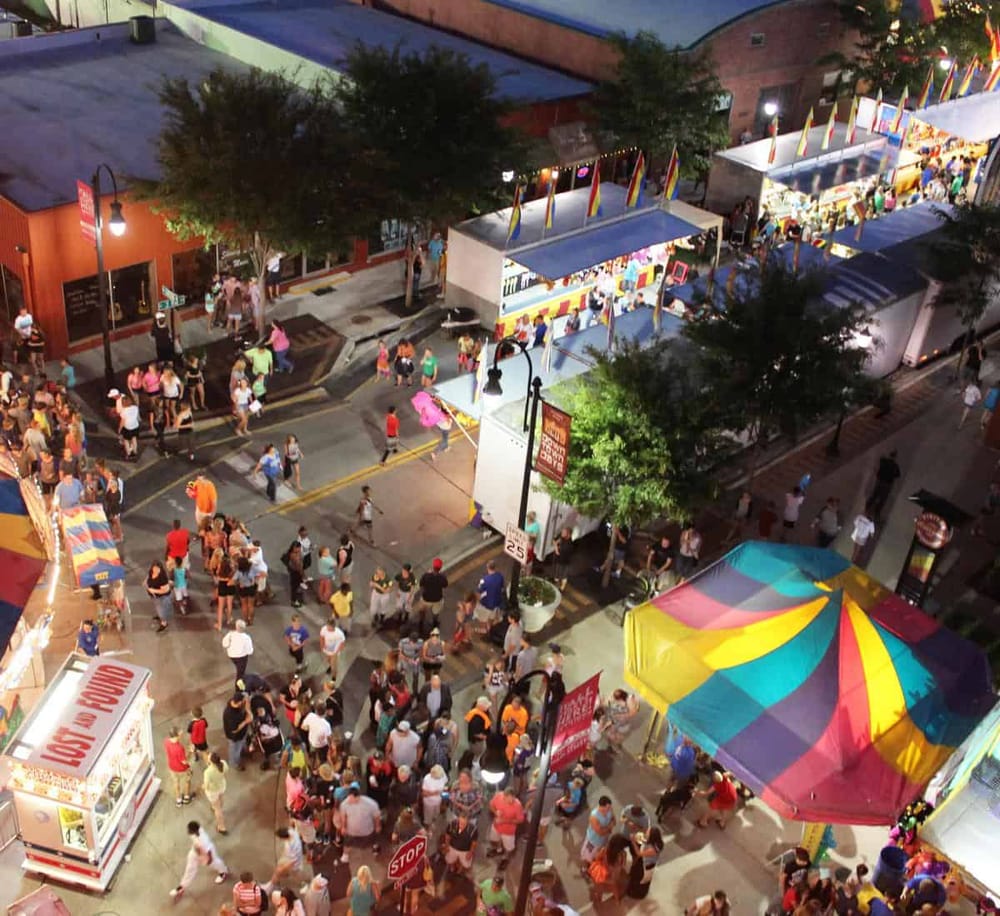 Crowd at night market festival with colorful tents and flags, lively street scene, and vibrant event atmosphere.