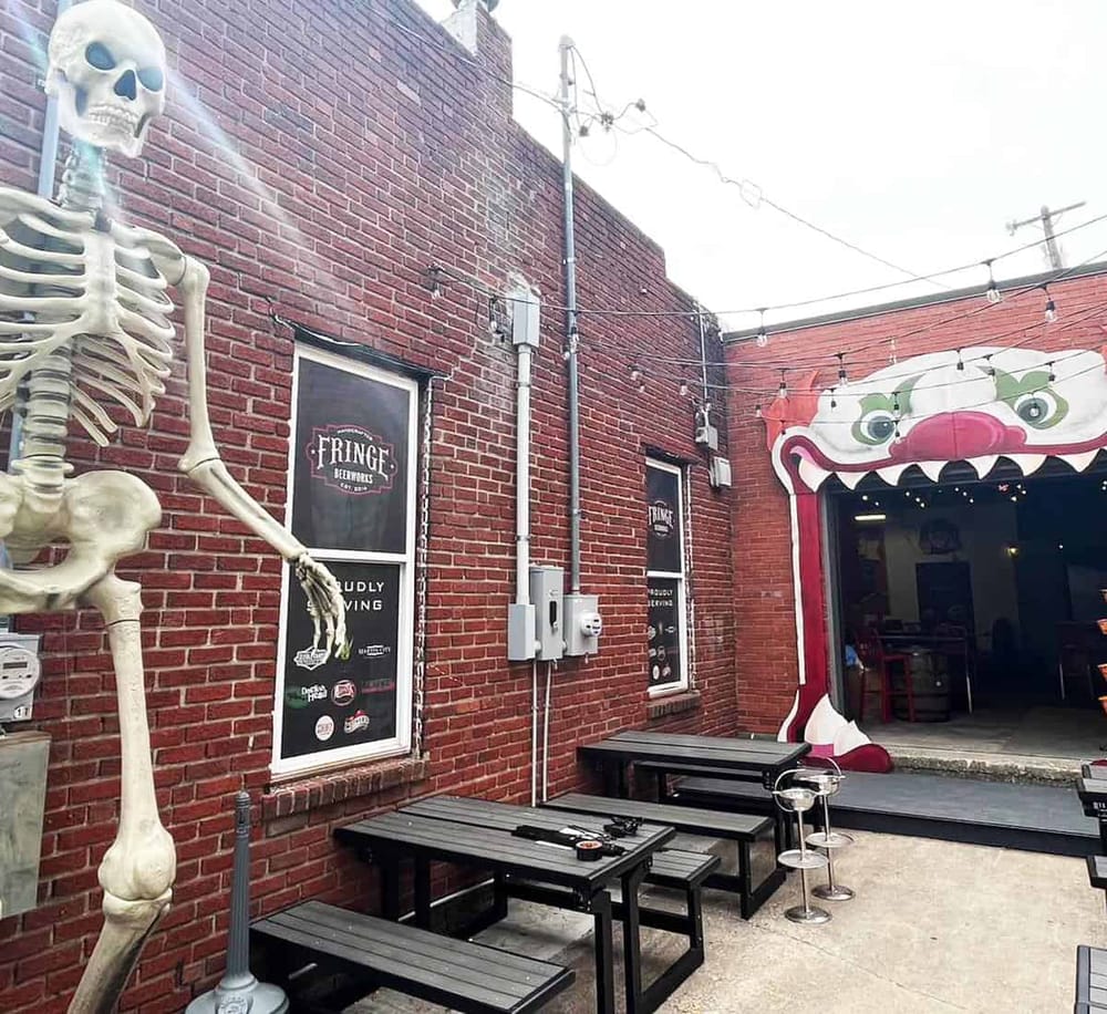 Skeleton and festive dragon mouth entrance at Quest For Directions brewery patio, outdoor seating, brick wall decor, casual dining atmosphere.