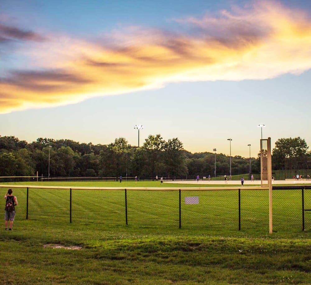 Broadcaster baseball fields at sunset with players and scenic sky view.