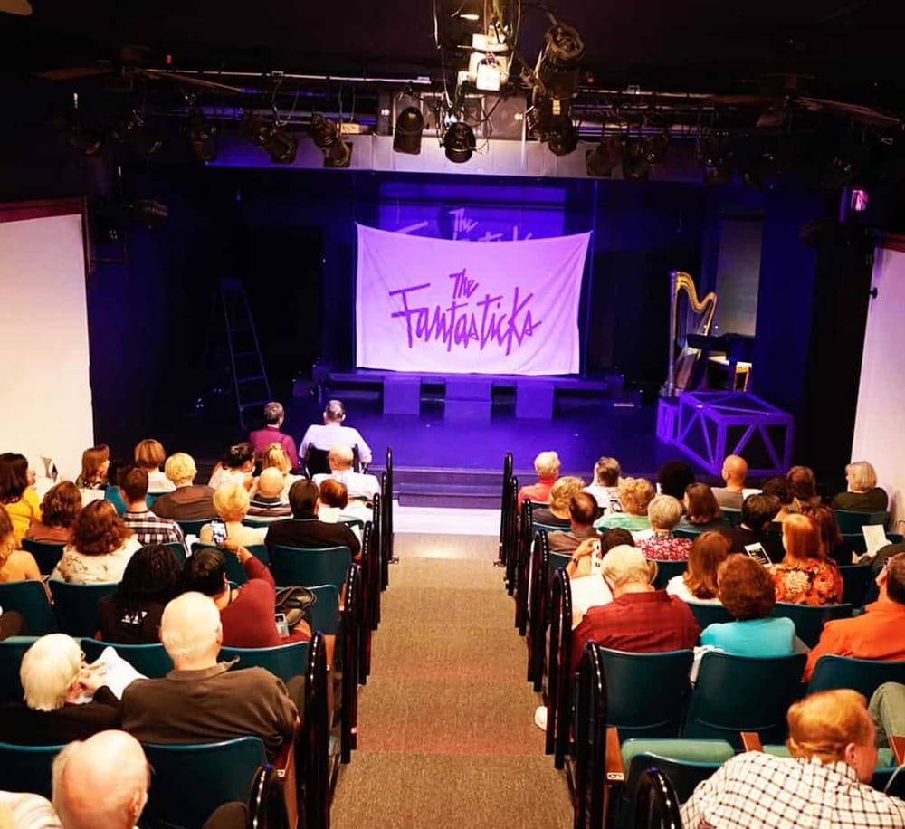 Broadway-style theatrical performance on stage at Quest For Directions event venue, with audience watching a show titled "The Fantasticks" in theater setting.