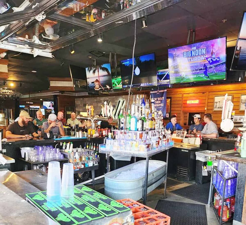Vibrant bar scene at Quest For Directions sports bar with multiple TVs and patrons enjoying drinks.
