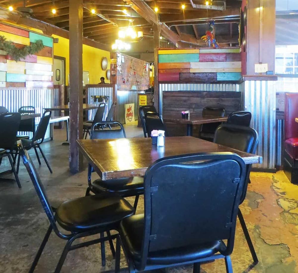 Colorful rustic restaurant interior with wooden tables and black chairs, vibrant wall decor, cozy ambiance, ideal for dining out.