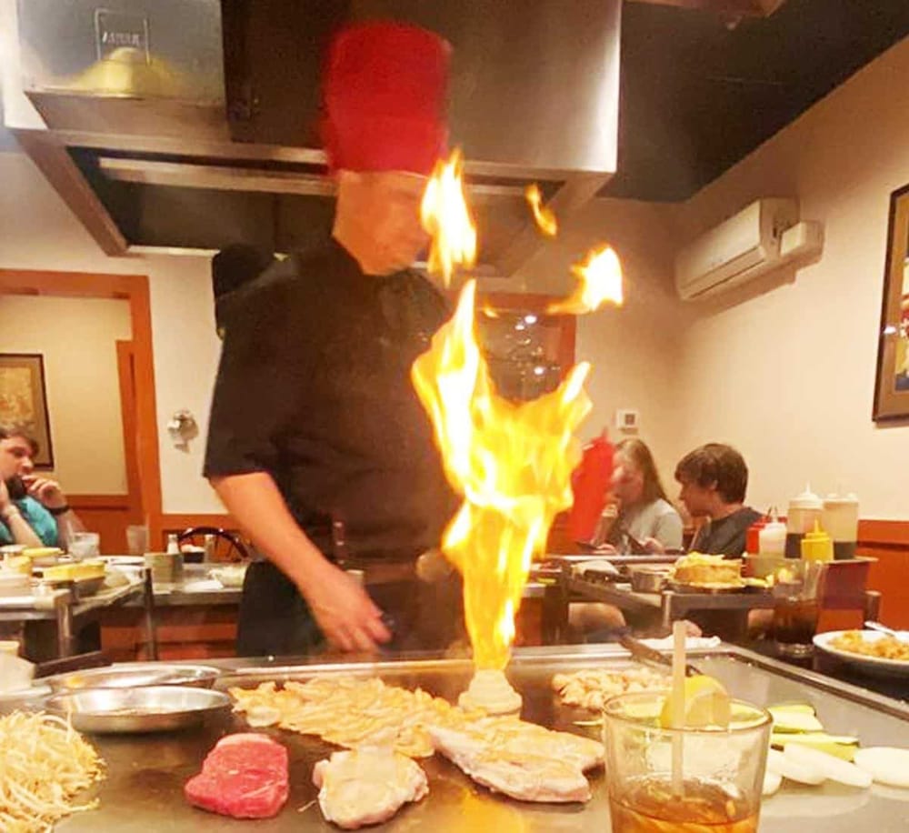 Flame chef at Japanese teppanyaki restaurant cooking steak and vegetables for a lively dining experience.