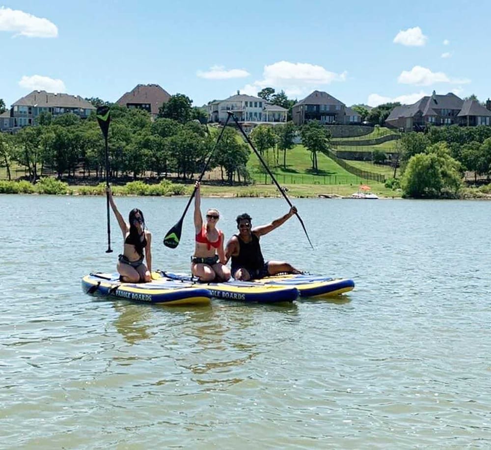 Kids paddleboarding on lake with scenic residential neighborhood in background.