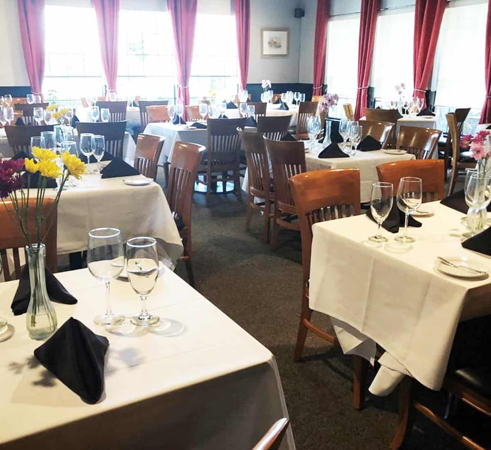 Elegant dining room setup with white tablecloths, floral centerpieces, and glassware for event venues.