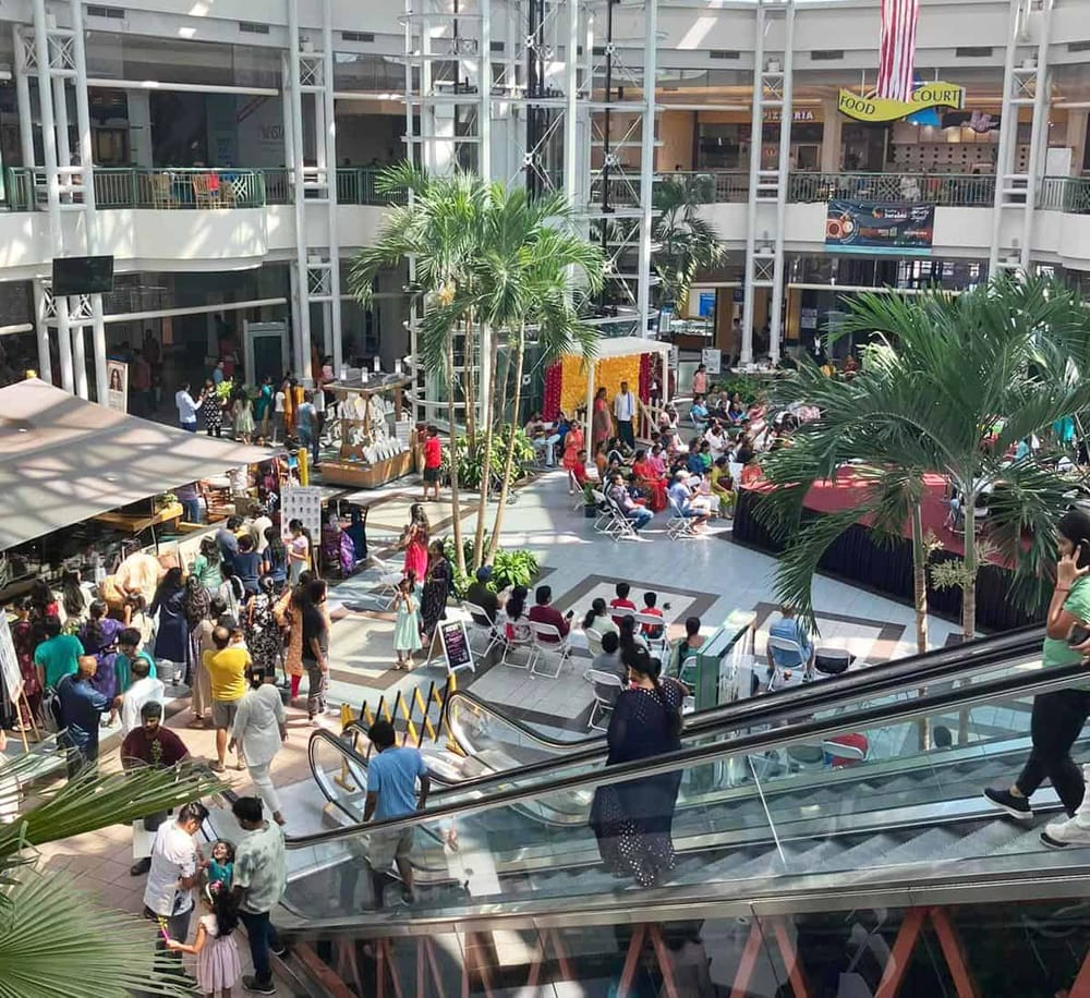 Vibrant shopping mall with indoor plant decor and bustling crowd in a modern retail space.