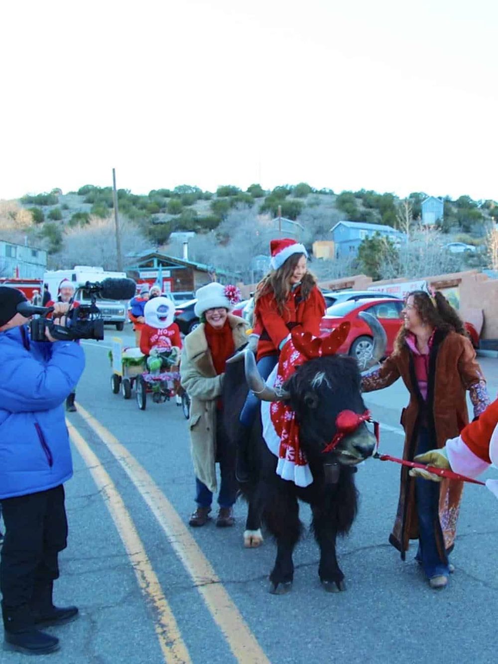 Colorful Christmas parade featuring people riding a decorated buffalo, capturing holiday community spirit.