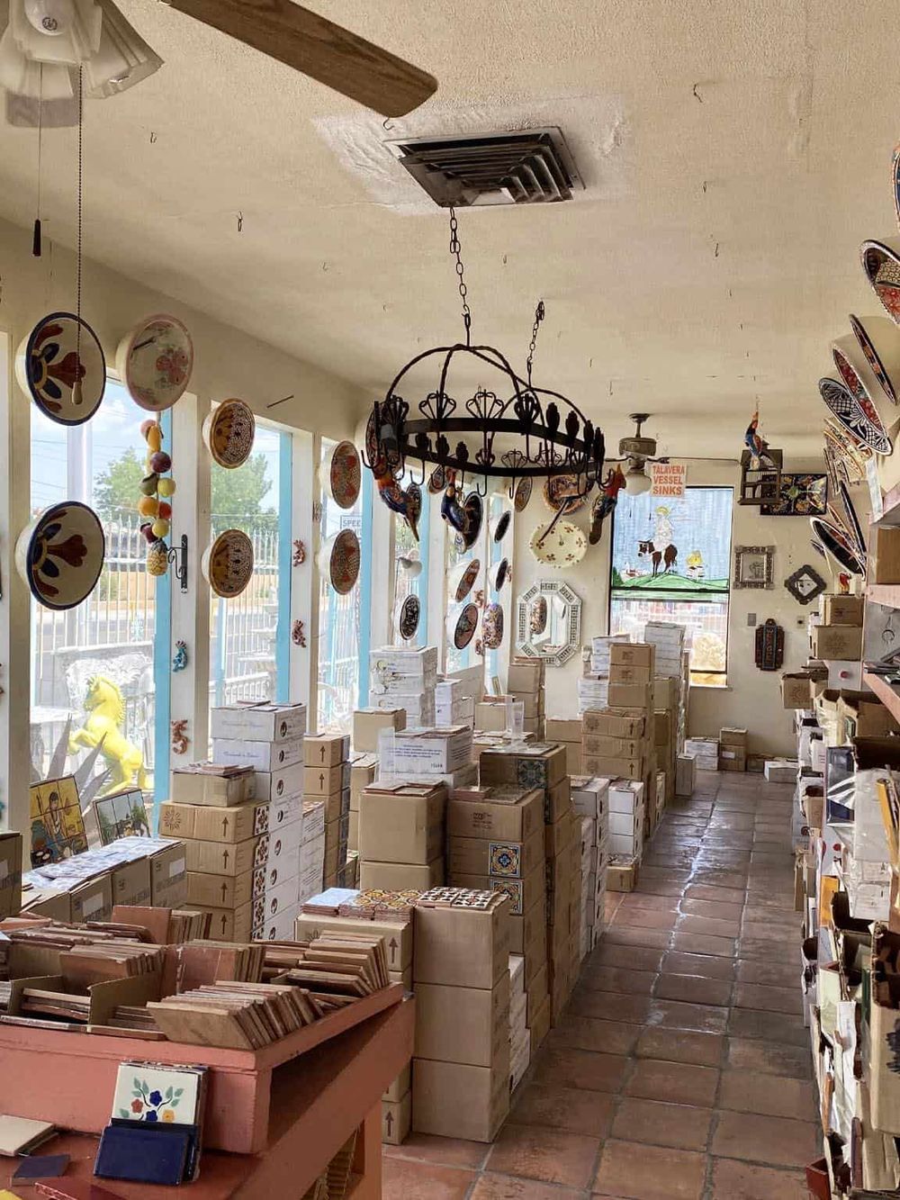 Colorful ceramic plates hanging in a quaint ceramic shop with stacks of boxes and artwork.