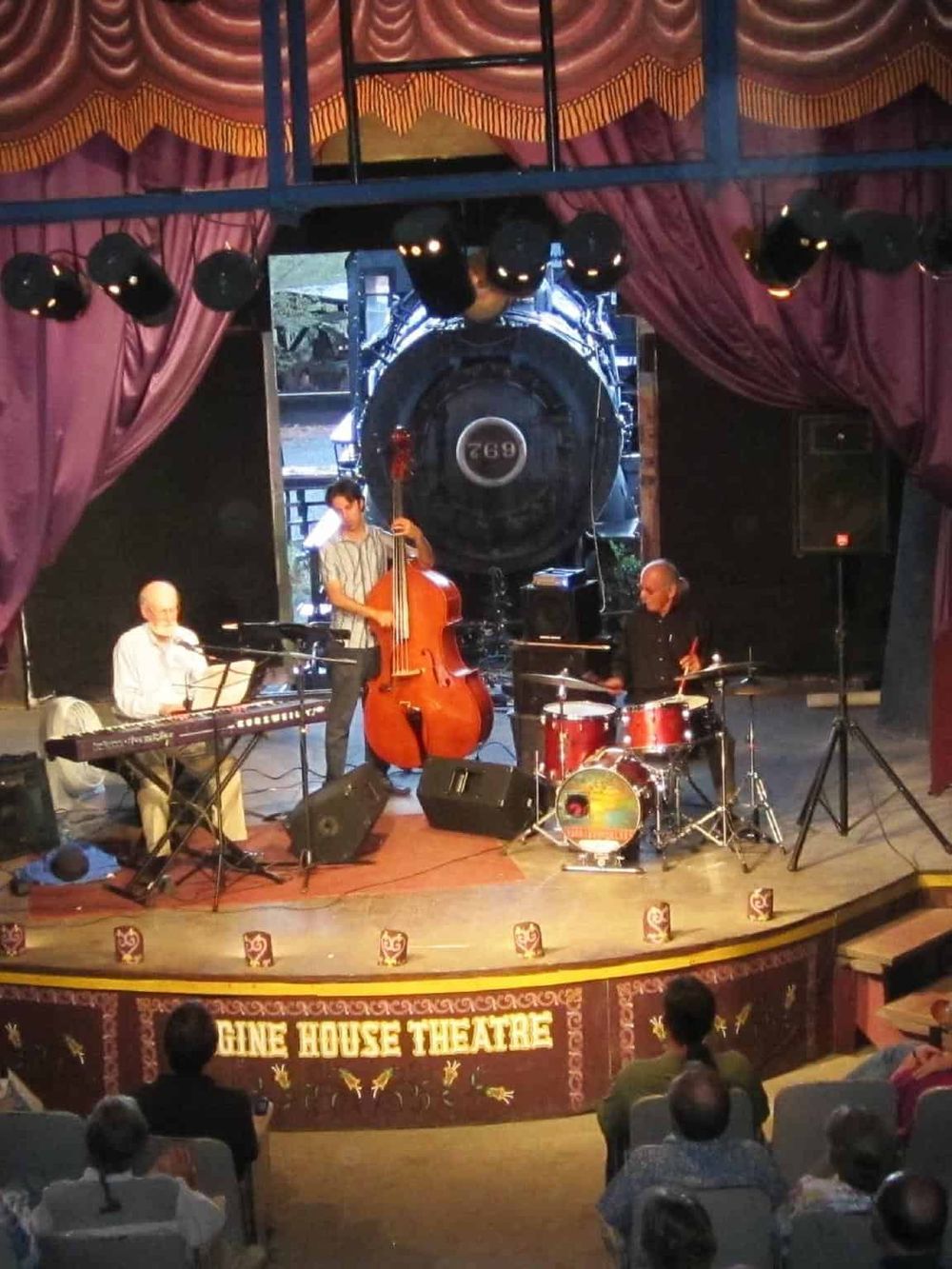 Live jazz band performing at a cozy, vintage theater with an audience enjoying the music.