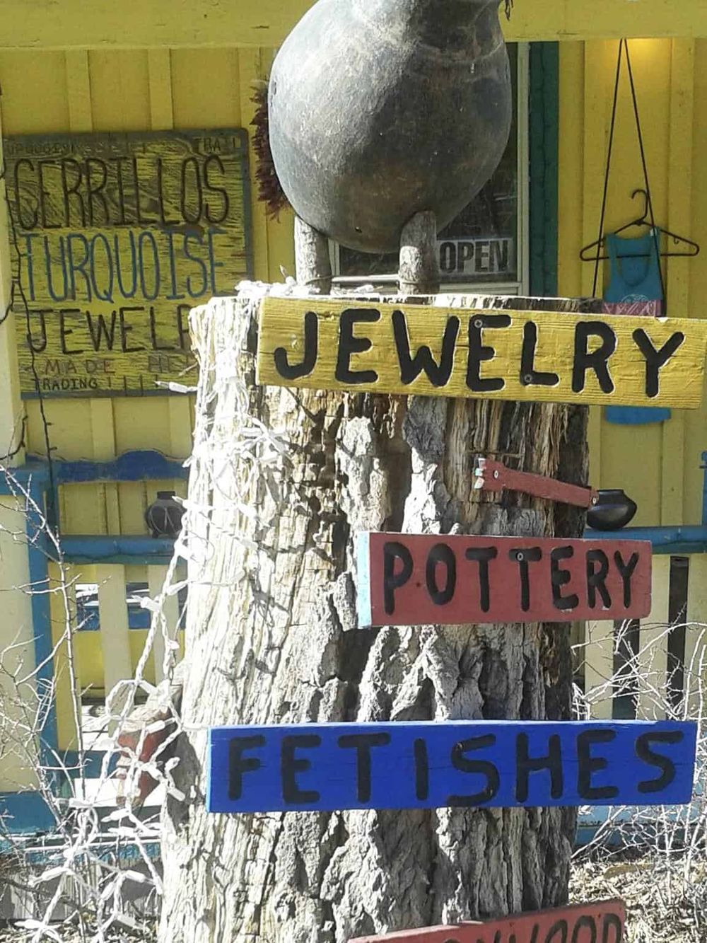 Colorful signs advertising jewelry, pottery, fetishes, and more at a rustic outdoor shop.
