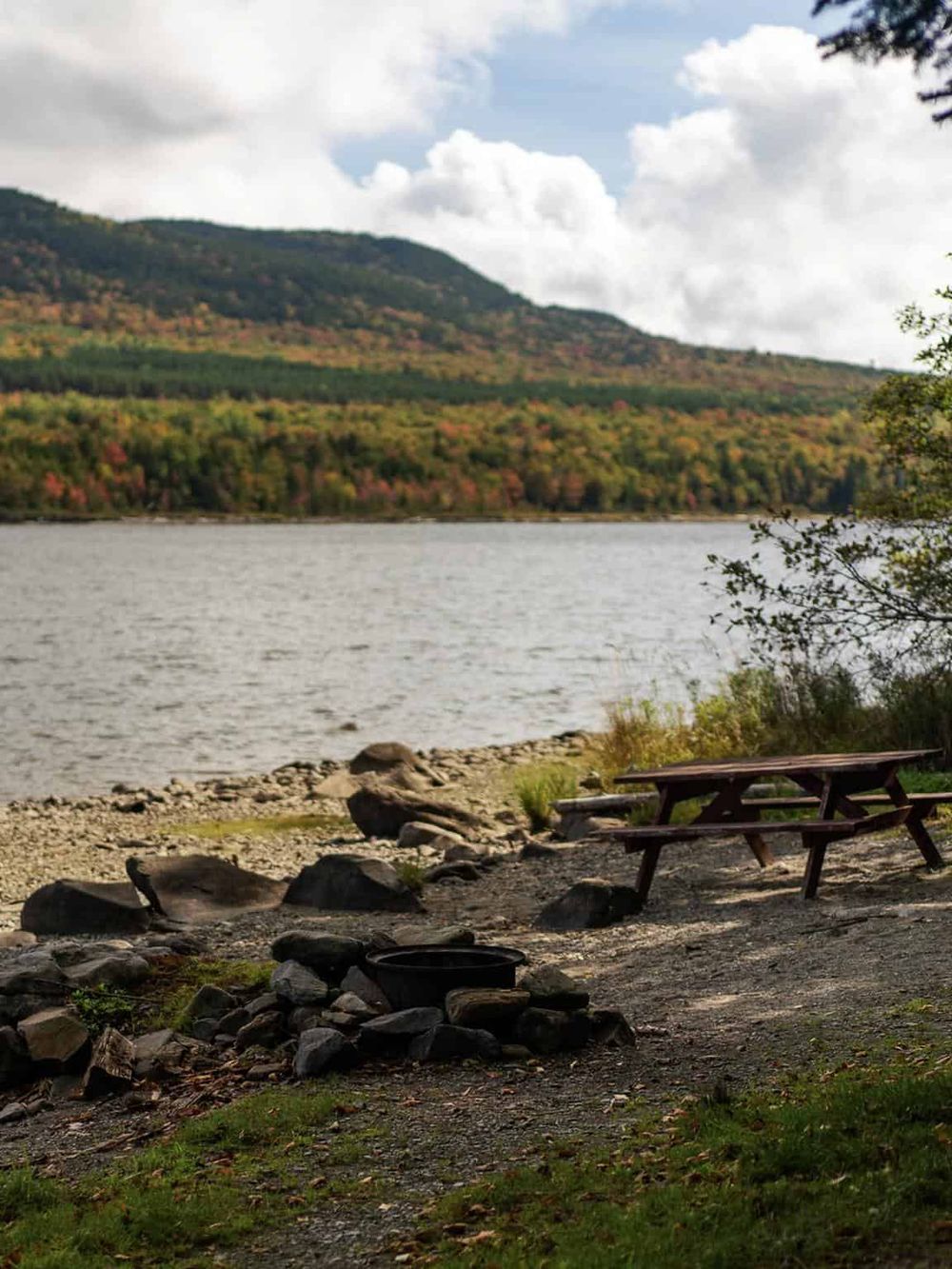 Serene lakeside scene with mountains, trees, and camping area at QuestForDirections, perfect for outdoor adventure.