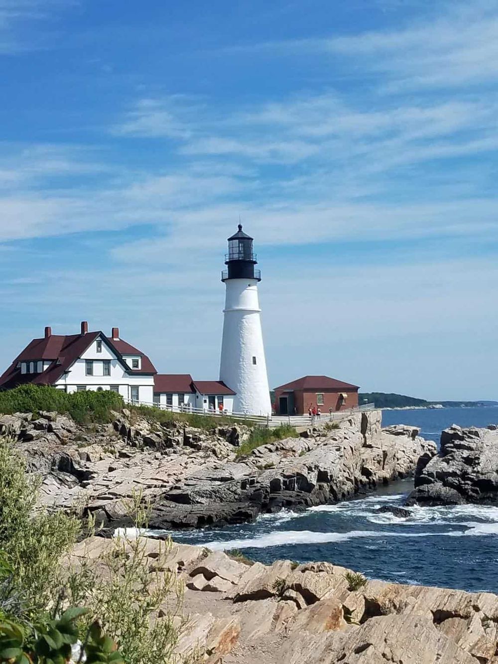 Lighthouse by the rocky coast, iconic lighthouse and surrounding buildings under blue sky.