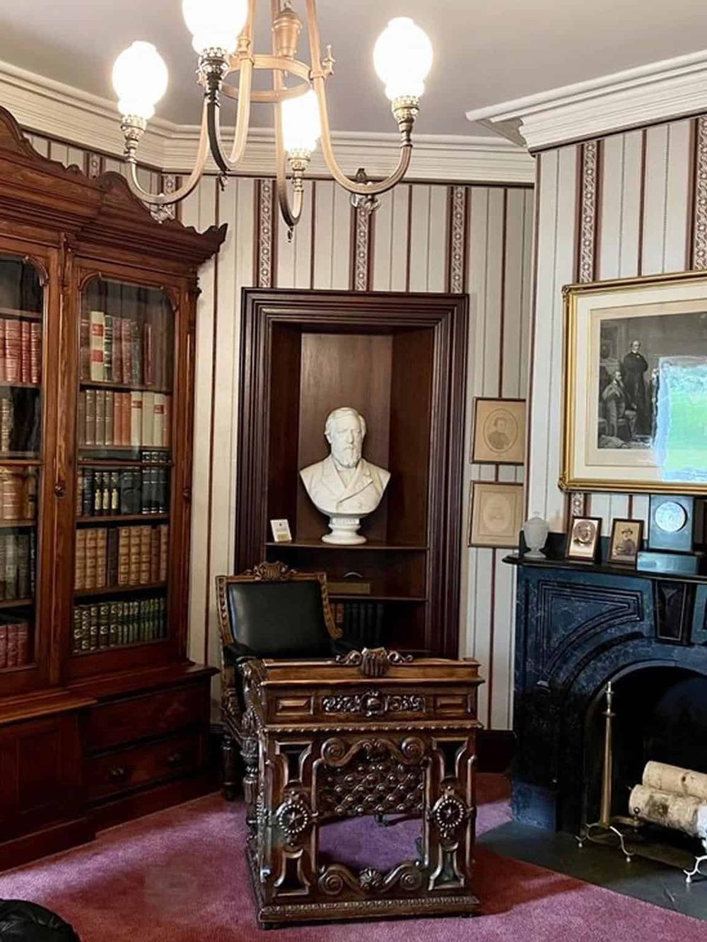 Antique study room with vintage furniture, portrait bust, and wooden bookshelves, reflecting classic interior design.