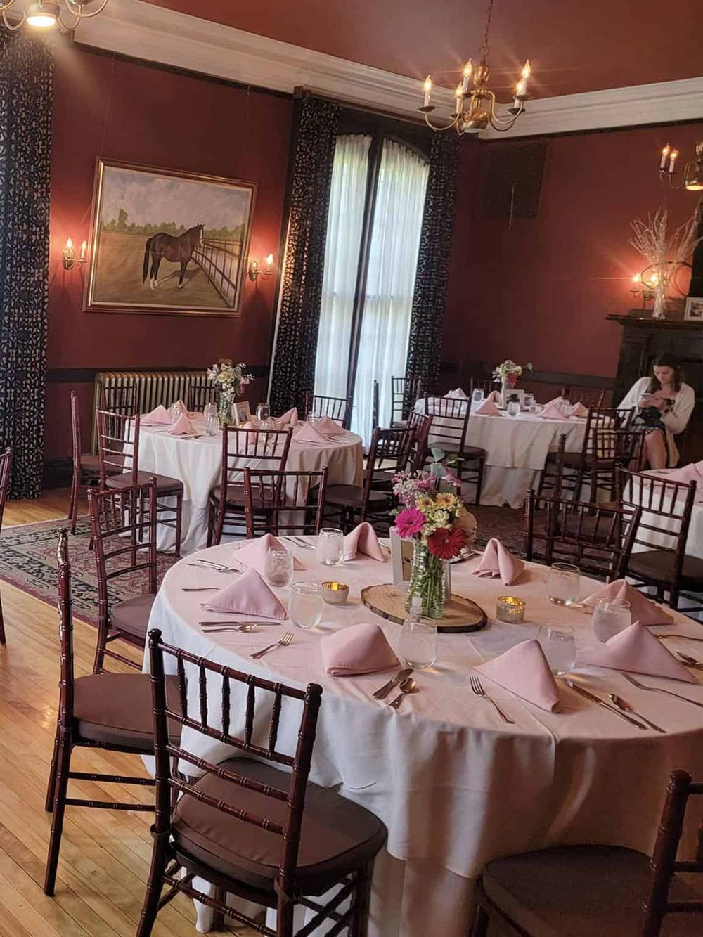 Elegant event venue decorated for a formal dinner with round tables, pink napkins, floral centerpieces, and ambient lighting.