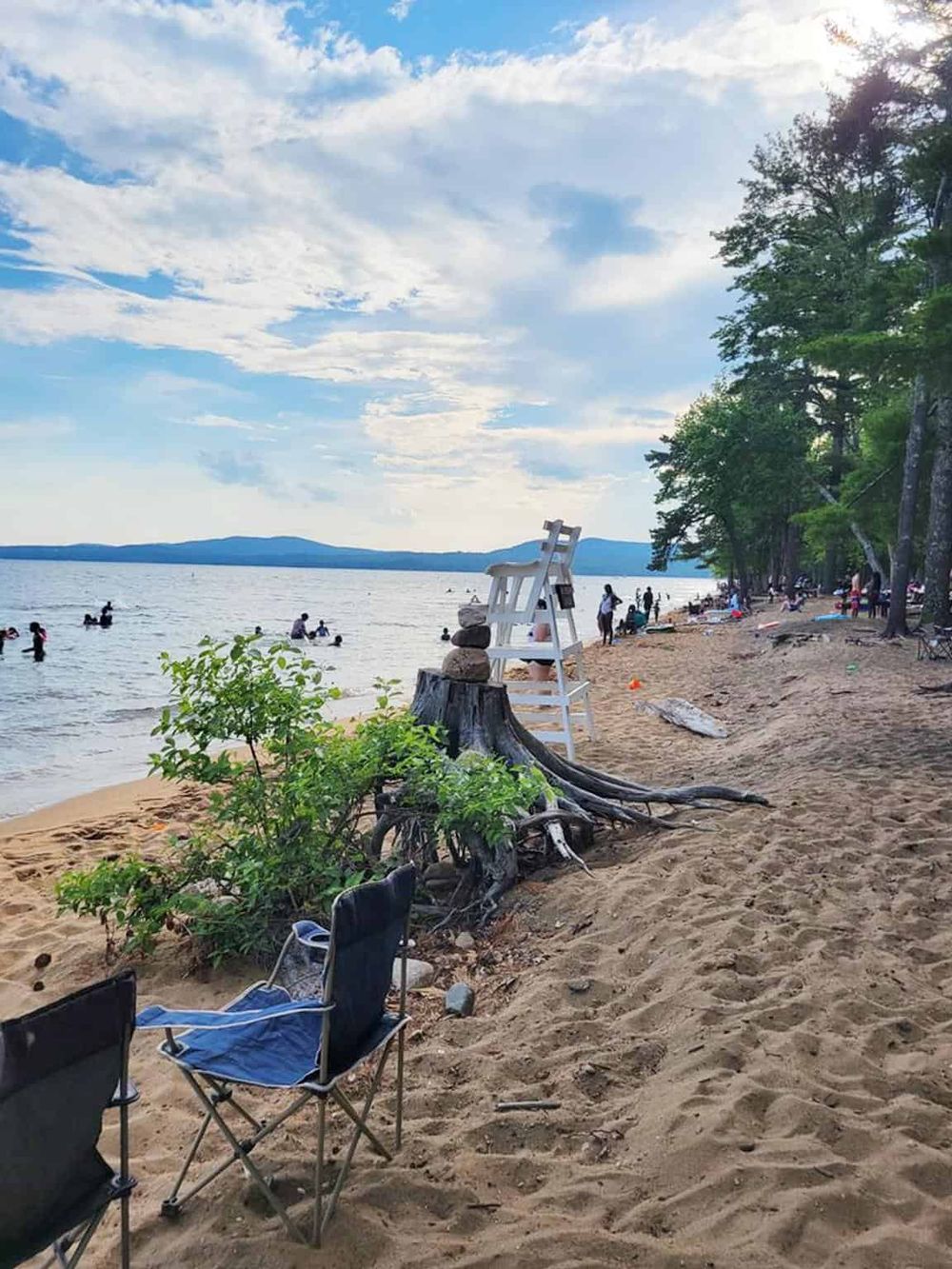 Relaxing lakeside beach scene with greenery, boaters, and a lifeguard chair, perfect for outdoor recreation and lake adventures.